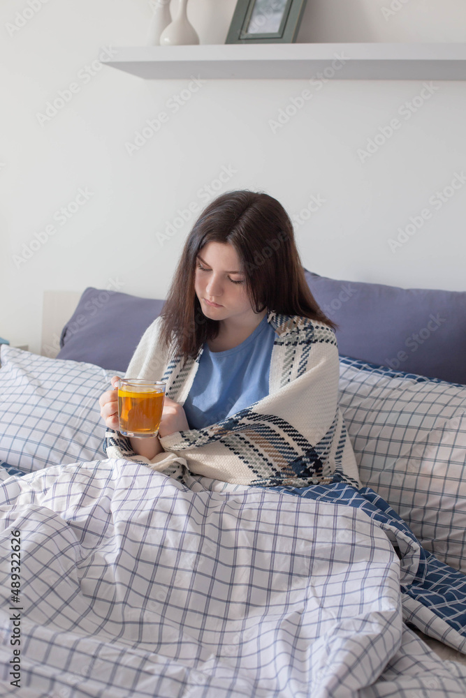 sick teen girl with tea on bed in white room