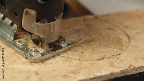 Artisan sawed OSB board with jig saw in circle leaving sawdust, closeup. Builder works by sawing osp board with fretsaw on circular marking photo