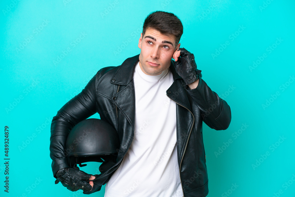 Naklejka premium Young caucasian man with a motorcycle helmet isolated on blue background frustrated and covering ears