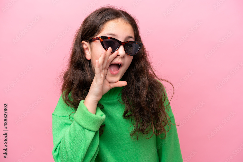 Fototapeta premium Little caucasian girl wearing sunglasses isolated on pink background shouting with mouth wide open