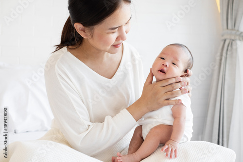Tablou pe pânză Portrait of young Asian mother and burping baby in bedroom