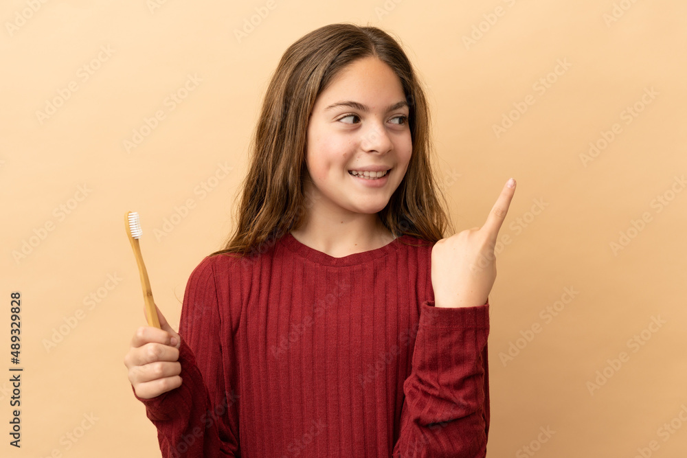 Little caucasian girl brushing her teeth isolated on beige background intending to realizes the solution while lifting a finger up Little caucasian girl brushing her teeth isolated on beige background intending to realizes the solution while lifting a finger up