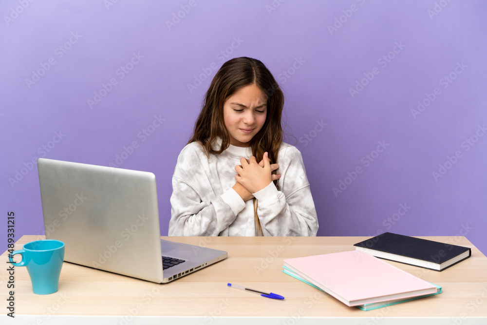 Little student girl in a workplace with a laptop isolated on purple background having a pain in the heart Little student girl in a workplace with a laptop isolated on purple background having a pain in the heart