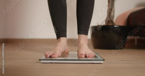Woman stepping on and off scale. Girl wiggling with foot toes while standing on scale checking her weight after workout.