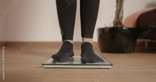 Young woman stepping on scale to check her weight and see results of workout sessions