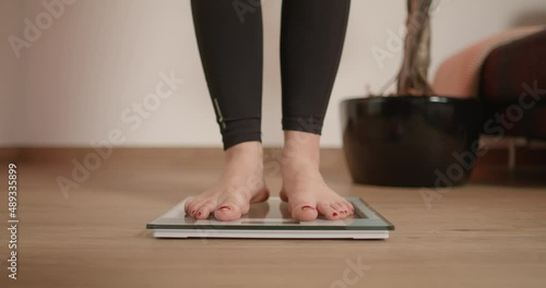 Young woman stepping on scale and wiggling her toes while checking her weight after workout and fitness photo