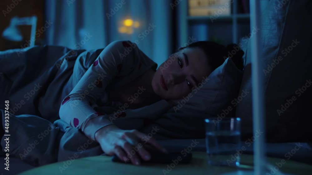 sleeping, bedtime and people concept - teenage girl lying in bed awaking because of smartphone at home at night sleeping, bedtime and people concept - teenage girl lying in bed awaking because of smartphone at home at night