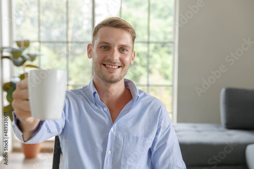 Portrait shot millennial caucasian male businessman in casual outfit sitting smiling look at camera in front of computer waving hand say hello greeting customer in webinar video distance conference