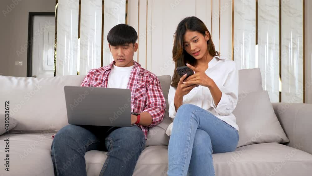 Slow motion shot, Young couple sitting on sofa in living room, young man working on laptop, Beautiful woman playing to young man's cell phone, he was annoyed and disinterested, she was not satisfied Slow motion shot, Young couple sitting on sofa in living room, young man working on laptop, Beautiful woman playing to young man's cell phone, he was annoyed and disinterested, she was not satisfied