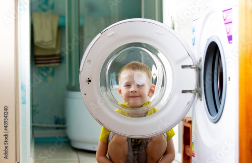 Little funny boy sits and looks out the window of the washing machine in the bathroom