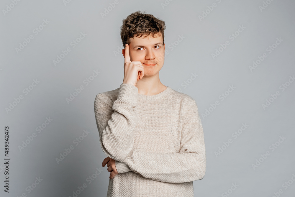 Photo of creative teenager boy pointing a finger at the temple while standing over gray background. Concept of thinking Photo of creative teenager boy pointing a finger at the temple while standing over gray background. Concept of thinking