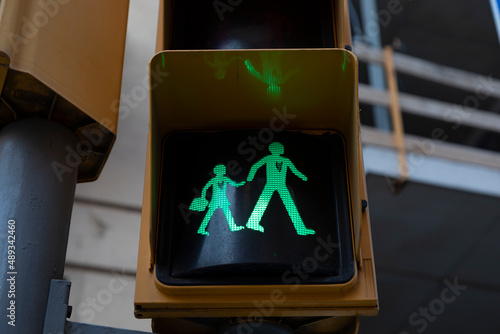 A green traffic light, indicating forward, at a crosswalk in a school zone, shows the figure of a child and an adult walking hand in hand