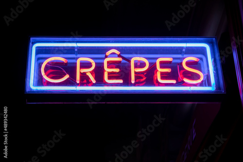 A crepe store with a bright neon blue and red sign glows in the dark on a street in Barcelona, Spain