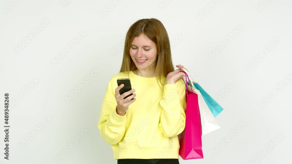 Young woman holding shopping bags while using mobile phone isolated on background Young woman holding shopping bags while using mobile phone isolated on background