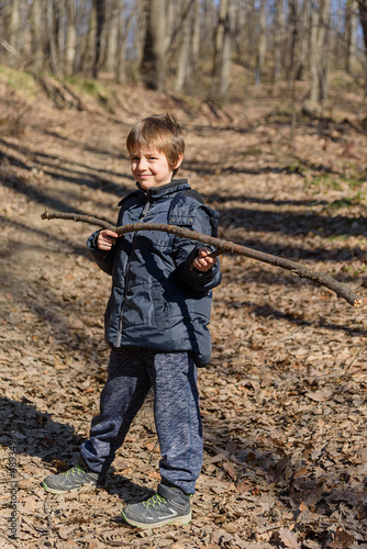 A boy is playing with a wooden stick in the woods
