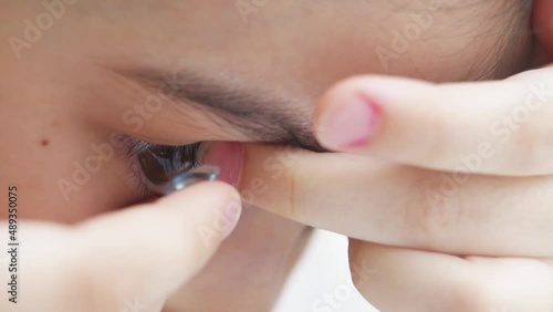 Close-up a little girl to put on contact lenses with fingers and blinks.  photo