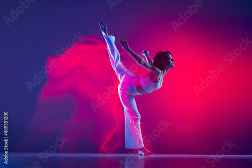 Young sportive beautiful girl, hip-hop dancer dancing hip hop isolated on purple background in pink neon light. Youth culture, style and fashion, action.
