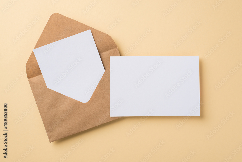 Top view of big brown craft envelope with two white postcards situated on beige isolated background blank space Top view of big brown craft envelope with two white postcards situated on beige isolated background blank space