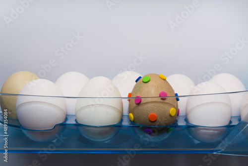 There are white eggs on the shelf in the refrigerator. One egg is creative. Easter concept photo