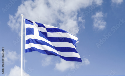 The Greek flag flying in the wind against the blue sky.