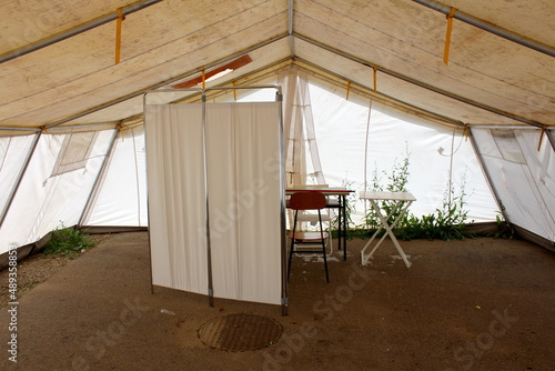 Inside of abandoned white field hospital tent built by military on paved parking lot and used for COVID-19 coronavirus outdoor testing with medical hospital ward screen next to portable plastic table 