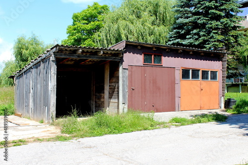 Row of three colorful dilapidated old rustic vintage makeshift garages made from metal sheets and wooden boards closed with two doors and small windows with broken glass next to paved road