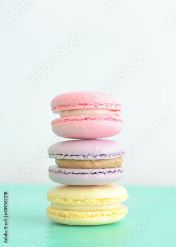 Stack of three macarons on light background. Delicious pink  purple and yellow macaroons. Vertical photo.