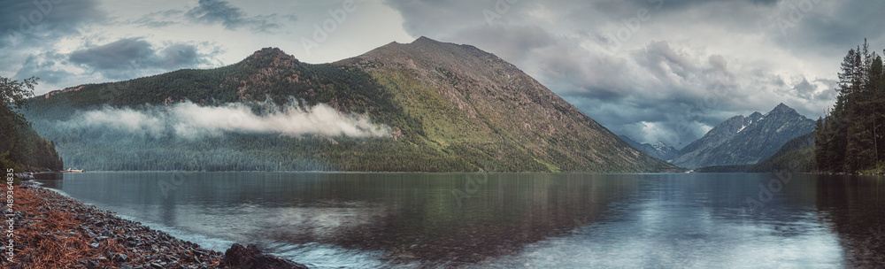 Panorama of the Lower Multinskoye Lake at dusk among the Altai Mountains in Russia. Background for traveling and hiking in the wild