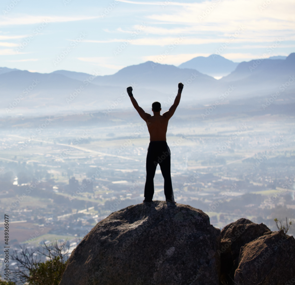 Hes reached the summit. Rearview of a man with his arms raised while standing on a mountain top. Hes reached the summit. Rearview of a man with his arms raised while standing on a mountain top.