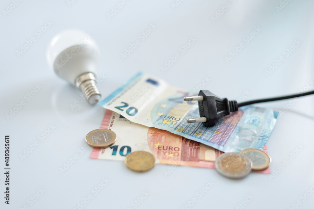 Black electric cap on euro banknotes and various coins, with a light bulb. Increased cost of electricity . Payment of electricity bills. Increasing the concept of electricity prices.