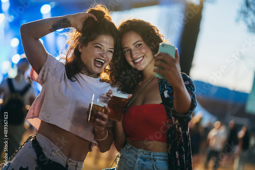 Two beautiful friends taking selfie with a samrtphone on a music festival photo