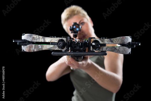 Foto Young woman shooting with crossbow isolated on black background.