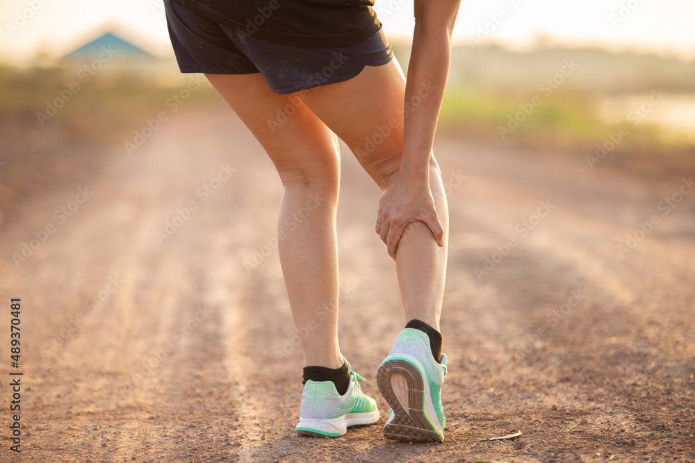 injury concept from exercise : Asian woman hands on thigh while running on park road. Shot in the morning, sunlight and warm effects. injury concept from exercise : Asian woman hands on thigh while running on park road. Shot in the morning, sunlight and warm effects.