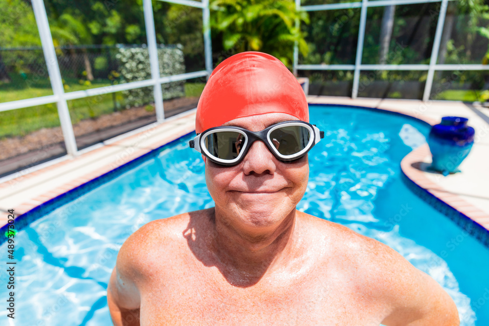 Senior man wearing swimming cap and goggles in pool looking at the camera with a big smile