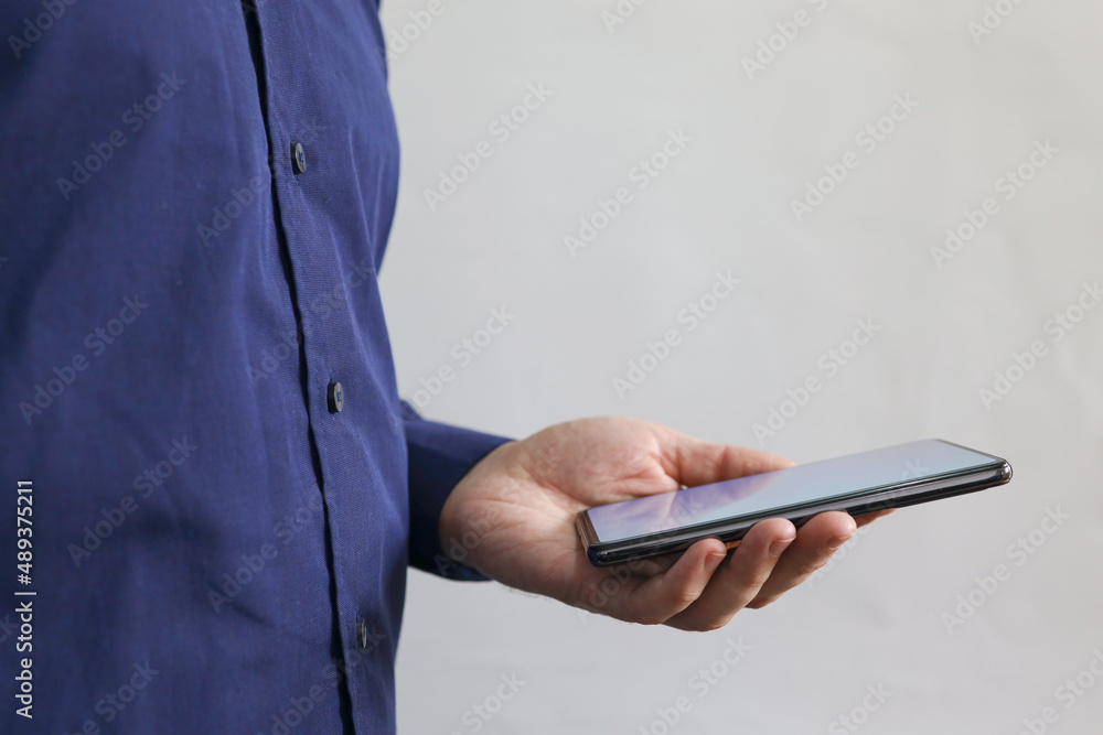 Man holding mobile phone in his hand. Man scrolling news or playing game. Business smart connection technology. Close-up of persons hand holding mobile phone with light screen. Man holding mobile phone in his hand. Man scrolling news or playing game. Business smart connection technology. Close-up of persons hand holding mobile phone with light screen.