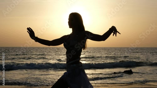 Silhouette of belly dancer woman dancing belly dance on a paradise beach at sunset