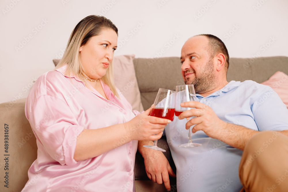 Happy caucasian couple relax on cozy sofa at home resting holding in their hands two glasses of wine and looking at each other with love. Happy caucasian couple relax on cozy sofa at home resting holding in their hands two glasses of wine and looking at each other with love.