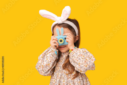 Canvas Print Cute kid girl is holding a small camera and taking a shot in a studio