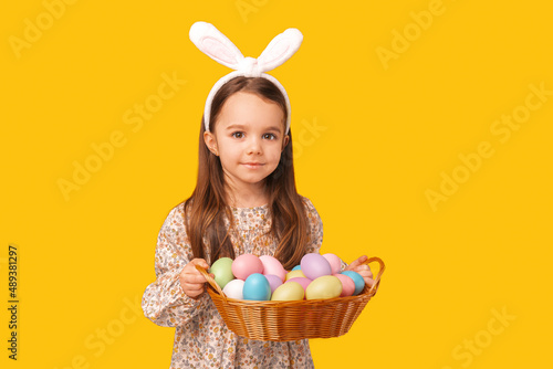 Close up portrait of a little girl holding a basket of colourful eggs.
