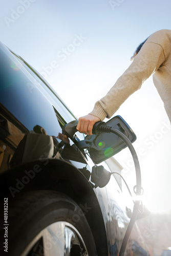 Canvastavla Woman's hand preparing to charge an electric car at city charging station