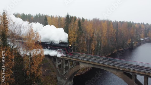 Steam locomotive with smoke from a chimney on a bridge over a river in Karelia