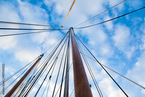 Mast of a sailing yacht without a sail. Bottom view on a background of blue sky with clouds.