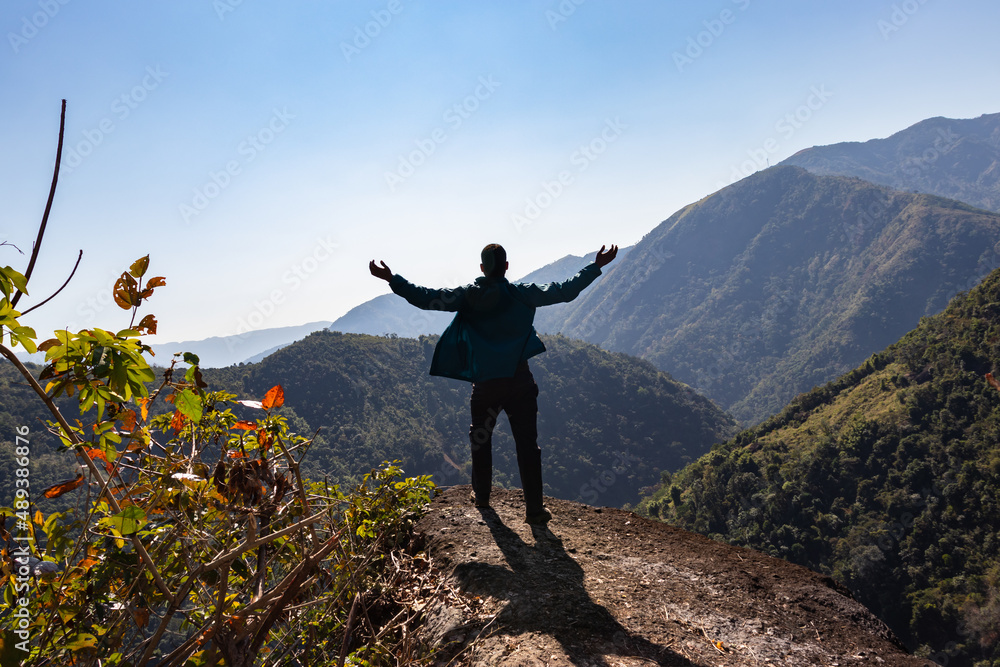 Obraz premium isolated young man at mountain top with green forests and misty blue sky at morning from flat angle