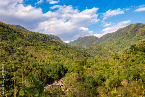 mountain valley covered with green forests and bright blue sky at afternoon from flat angle © explorewithinfo
