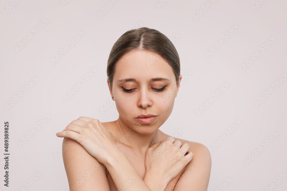 Portrait of a young attractive caucasian blonde woman with makeup touching the skin of her body isolated on a beige background. Beauty and fashion. Skin care Portrait of a young attractive caucasian blonde woman with makeup touching the skin of her body isolated on a beige background. Beauty and fashion. Skin care