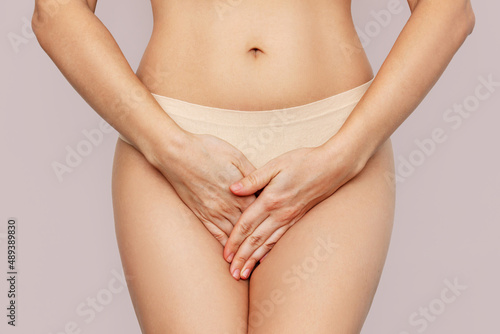 Valokuva Cropped shot of a young woman in underwear holding her crotch with her hands, suffering from cystitis isolated on beige background