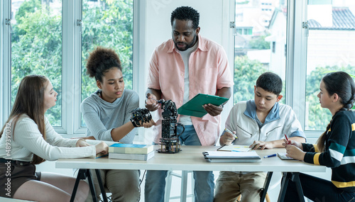 Obraz na plátne group of international students of Asian, African American youths and white girls sit and study with educational robot hands guided by teachers in school classrooms