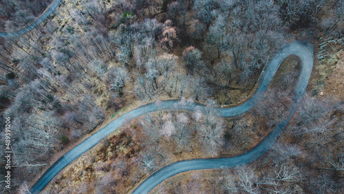 Aerial high angle view of narrow winding curvy mountain road among the trees in winter forest. Bird's eye view landscape.