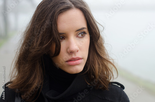 Portrait of a beautiful woman in black clothes outdoors on a misty winter day.