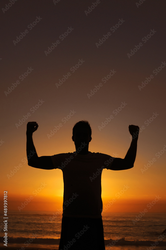 Finding the power within. Silhouette of a man standing with his arms victoriously raised against the sunset.